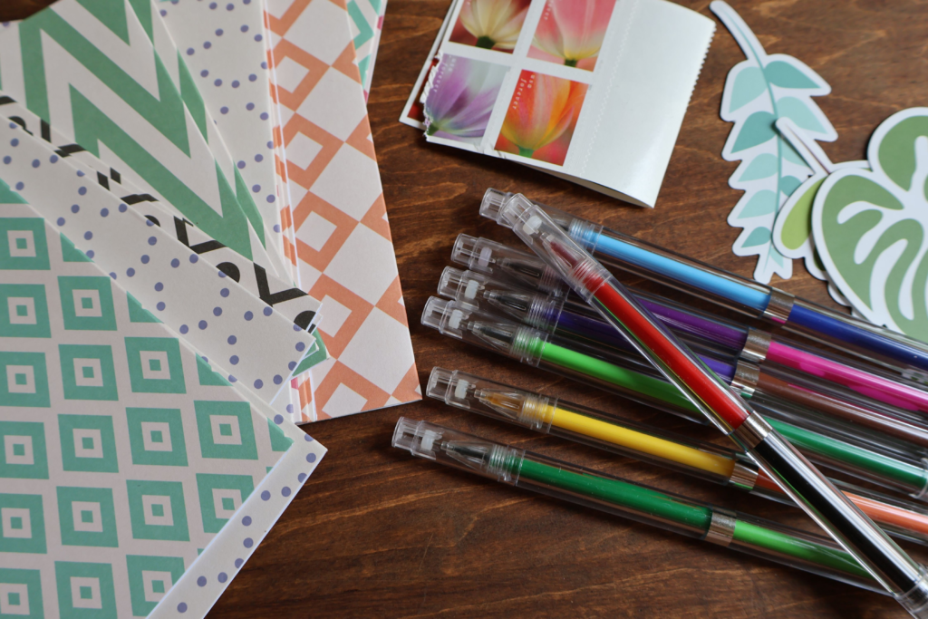 Colorful gel pens and patterned craft papers spread out on a wooden table, ready for scrapbooking or journaling.