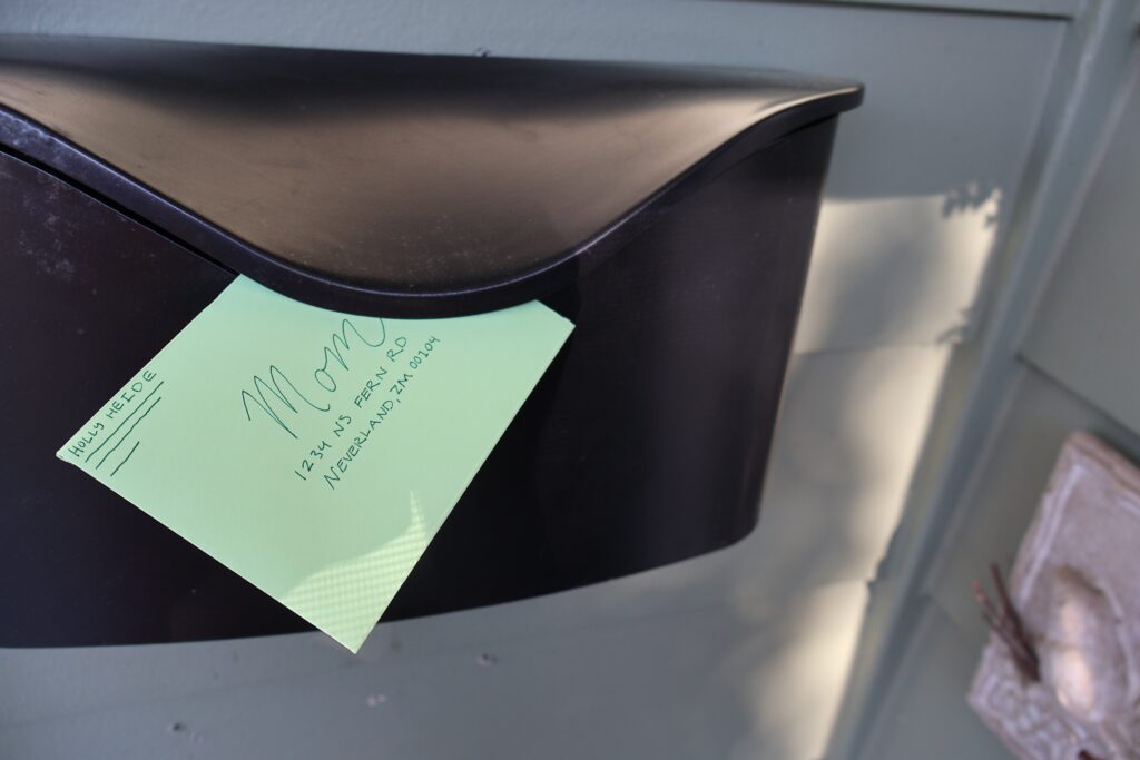 Mint-green envelope attached to a dark mailbox, featuring handwritten address details