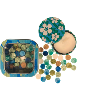 Holly Heide Ocean Mix sealing wax pearls in blue, green and metallic tones with decorative storage tin, candle and scattered wax pearls.